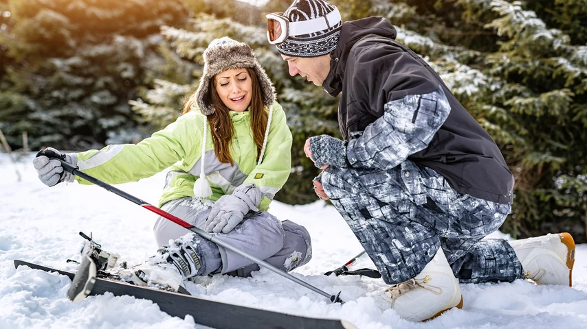 Young man snowboarder helps a beautiful young female skier who fell down on mountain slope.